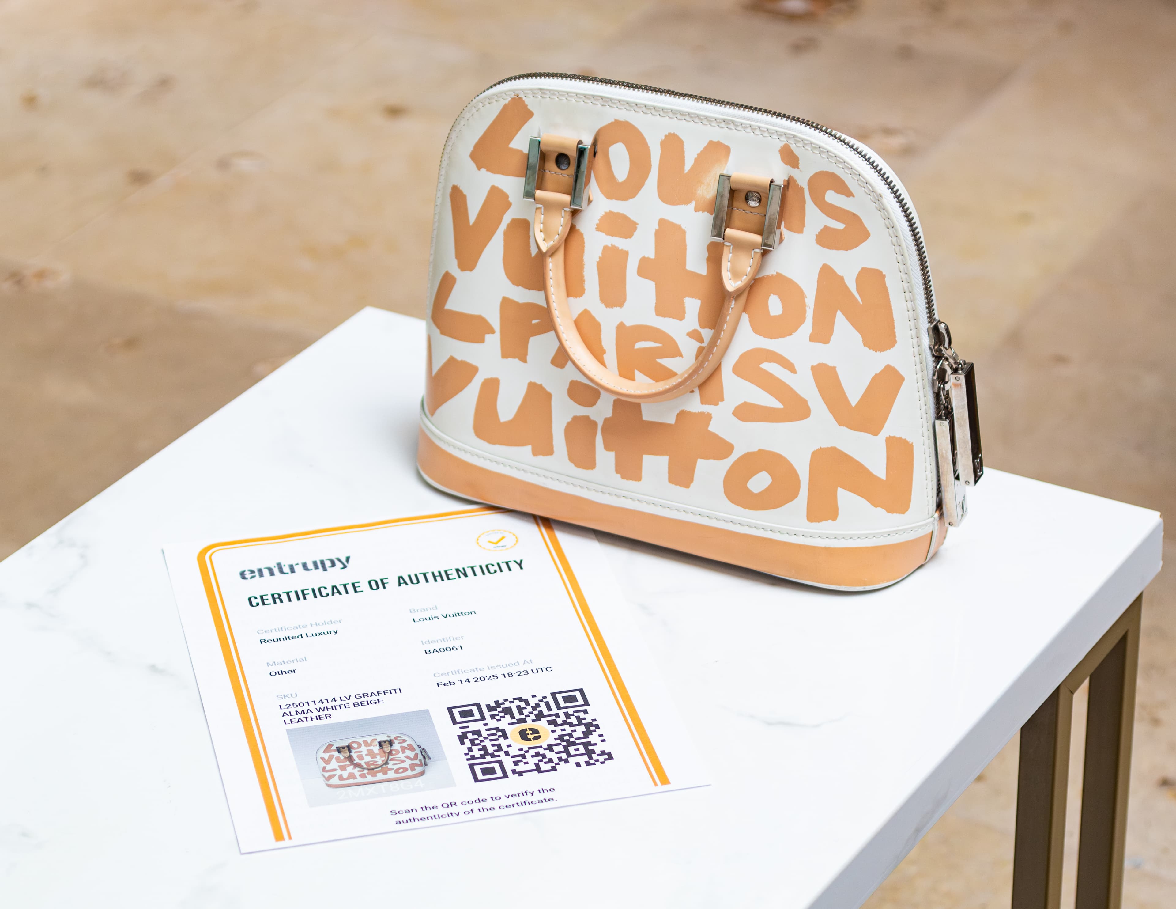 Louis Vuitton handbag with beige graffiti-style lettering on white table, accompanied by a certificate of authenticity.